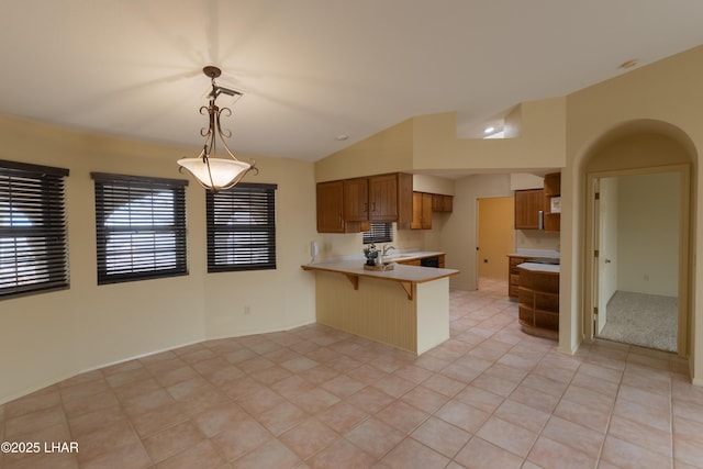 kitchen featuring brown cabinets, a sink, arched walkways, a peninsula, and light countertops