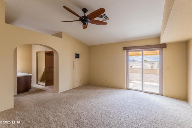 unfurnished room featuring visible vents, light colored carpet, lofted ceiling, arched walkways, and a ceiling fan