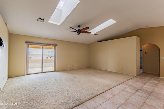 unfurnished room featuring visible vents, vaulted ceiling with skylight, arched walkways, light colored carpet, and ceiling fan