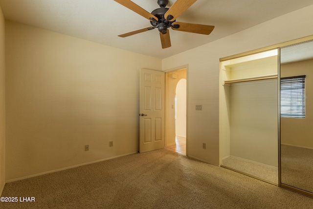 unfurnished bedroom featuring a ceiling fan, baseboards, carpet floors, arched walkways, and a closet