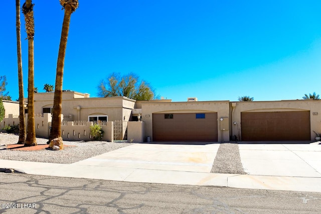 pueblo-style house featuring a fenced front yard, concrete driveway, a garage, and stucco siding