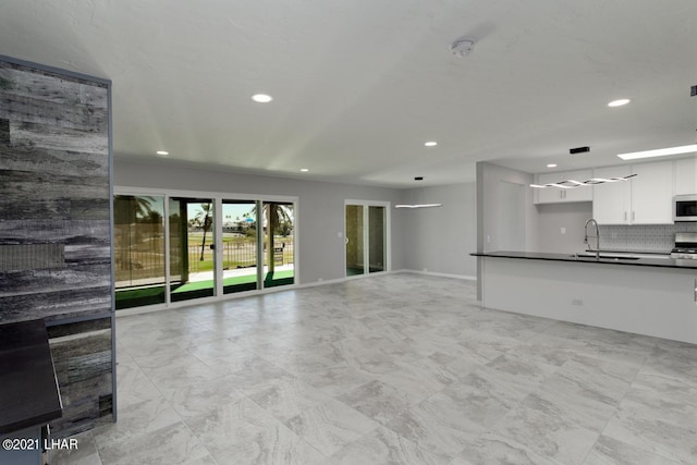 unfurnished living room with baseboards, a sink, and recessed lighting