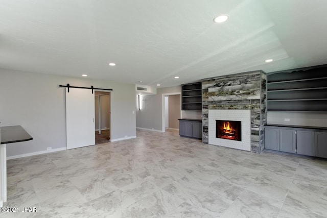 unfurnished living room with a barn door, baseboards, visible vents, a fireplace, and recessed lighting