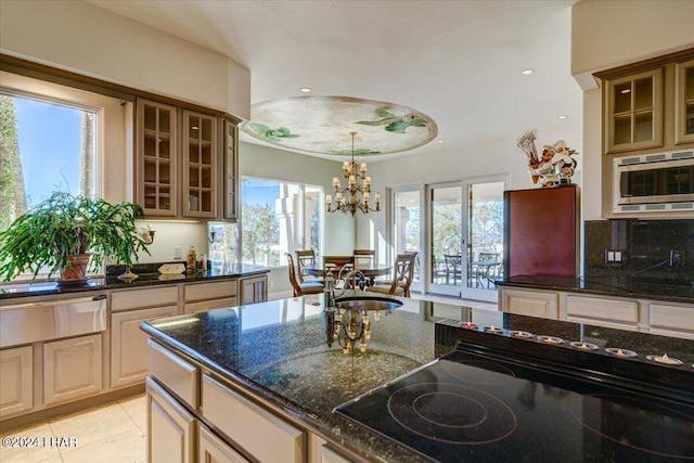 kitchen with dark stone countertops, an inviting chandelier, sink, stainless steel microwave, and a healthy amount of sunlight