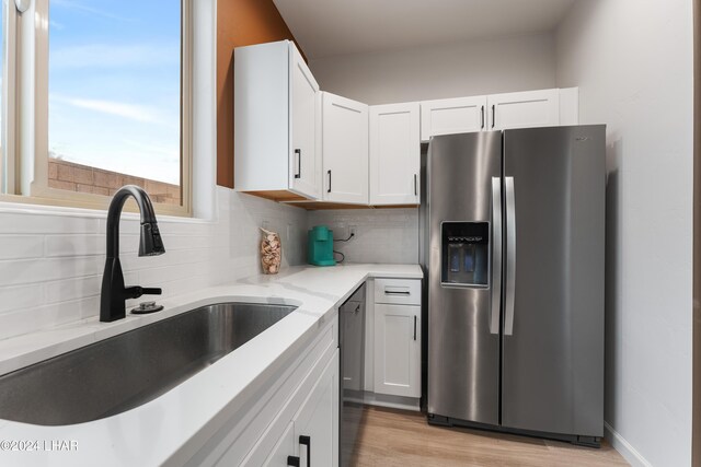 kitchen with sink, stainless steel fridge, white cabinetry, backsplash, and light stone countertops