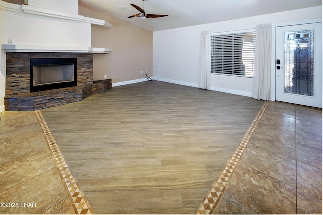 unfurnished living room featuring baseboards, a ceiling fan, lofted ceiling, wood finished floors, and a stone fireplace