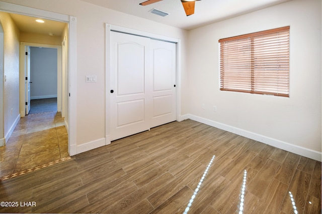 unfurnished bedroom with ceiling fan, wood finished floors, visible vents, baseboards, and a closet