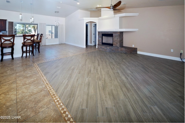 unfurnished living room featuring ceiling fan, a stone fireplace, wood finished floors, visible vents, and baseboards