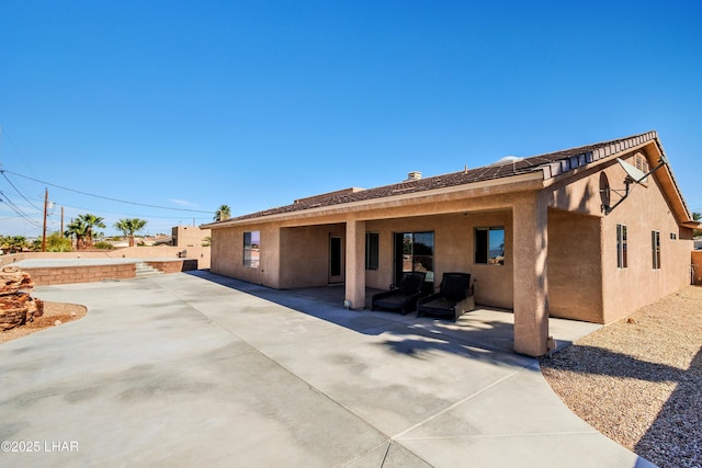 rear view of house with a patio area, fence, and stucco siding