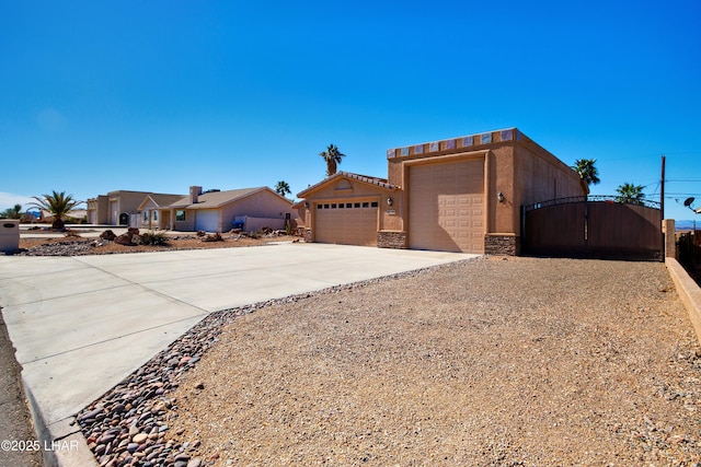 view of front of home with an attached garage, concrete driveway, stone siding, a gate, and stucco siding