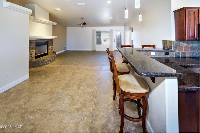 kitchen with arched walkways, a fireplace, a breakfast bar area, a ceiling fan, and open floor plan