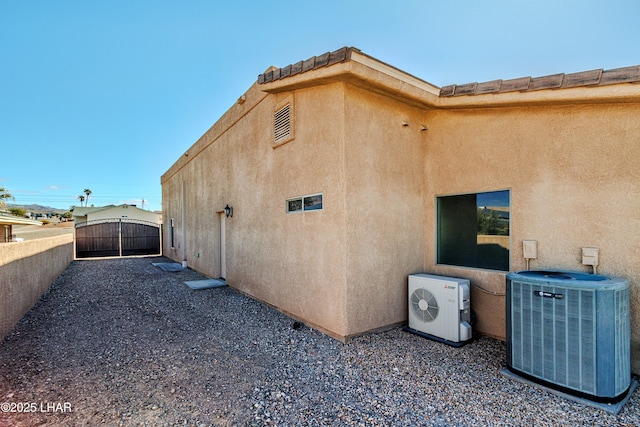 view of property exterior featuring central AC, a tile roof, a gate, stucco siding, and ac unit