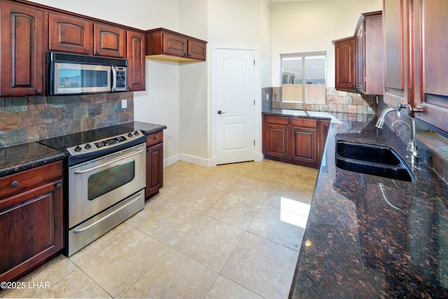 kitchen with light tile patterned floors, a sink, appliances with stainless steel finishes, dark stone counters, and tasteful backsplash