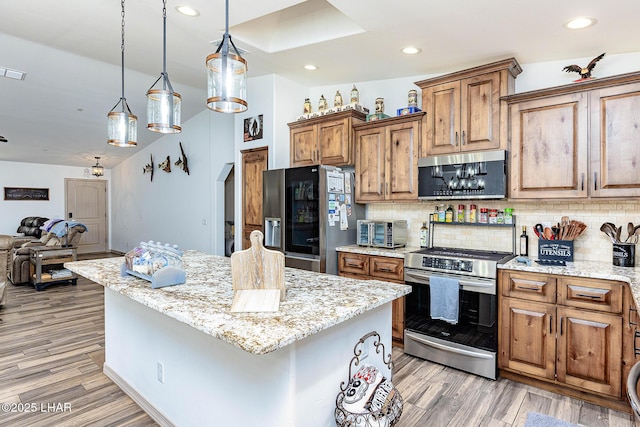 kitchen featuring open floor plan, appliances with stainless steel finishes, brown cabinetry, and light stone counters