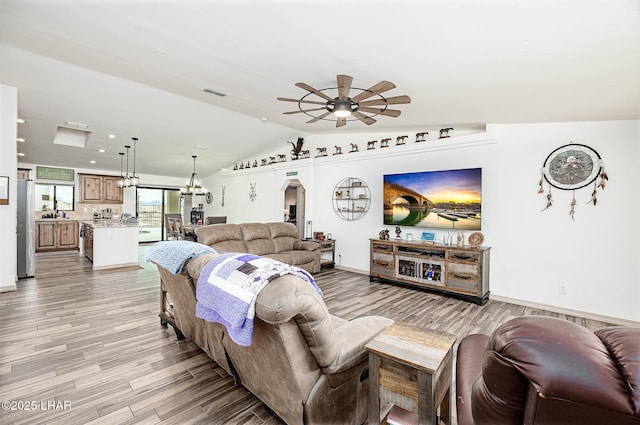 living room featuring arched walkways, ceiling fan with notable chandelier, light wood finished floors, and visible vents