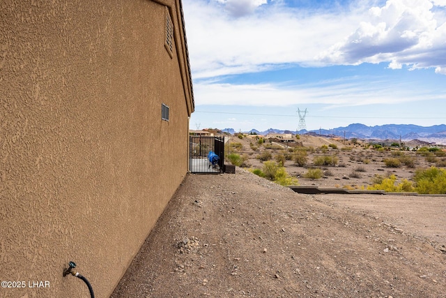 view of side of home featuring a gate, a mountain view, and stucco siding