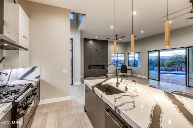 kitchen with decorative light fixtures, light stone countertops, sink, range with two ovens, and white cabinets