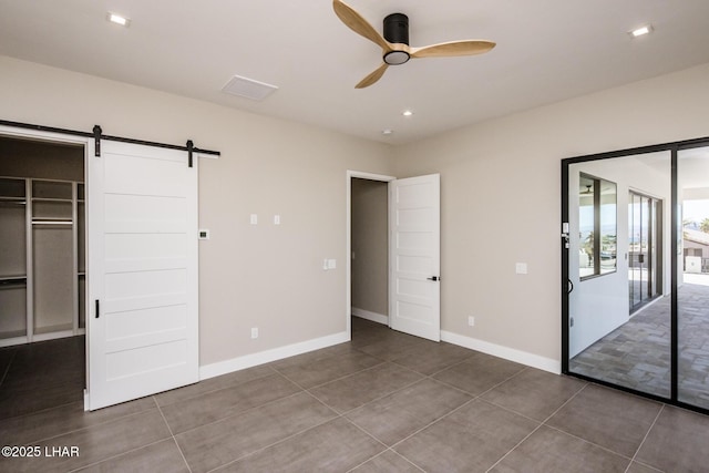 unfurnished bedroom with a closet, a walk in closet, dark tile patterned flooring, ceiling fan, and a barn door