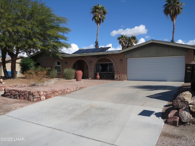 single story home featuring a garage, concrete driveway, brick siding, and solar panels