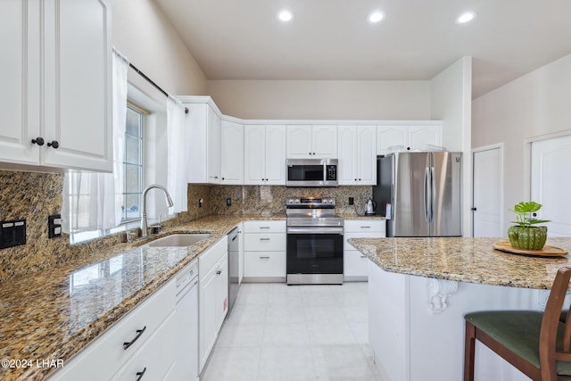 kitchen featuring appliances with stainless steel finishes, white cabinets, a sink, and light stone countertops