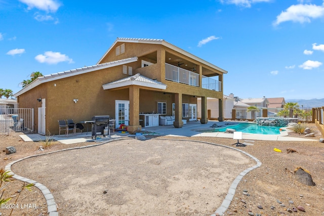 rear view of house with a patio, stucco siding, a pool with connected hot tub, fence, and a balcony