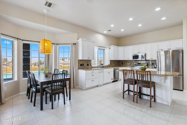 kitchen with light stone counters, stainless steel appliances, a kitchen island, visible vents, and white cabinetry