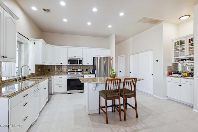 kitchen with appliances with stainless steel finishes, a center island, a sink, and light stone countertops