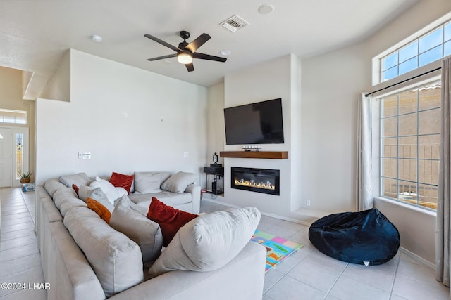 living room featuring light tile patterned floors, visible vents, baseboards, a ceiling fan, and a glass covered fireplace