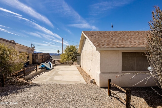 view of side of home featuring a shingled roof, a patio area, fence, and stucco siding