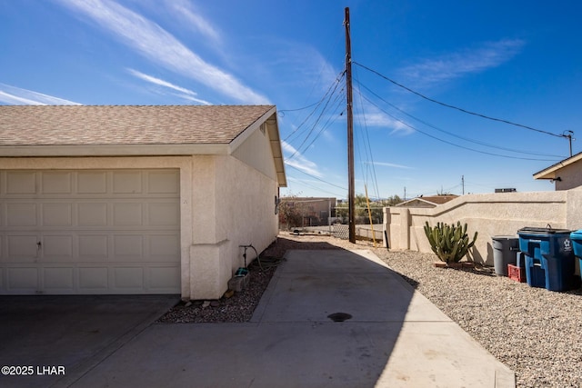 view of side of property featuring a garage, roof with shingles, fence, and stucco siding