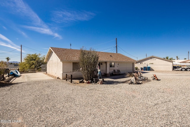 view of front facade with a garage, roof with shingles, fence, and stucco siding