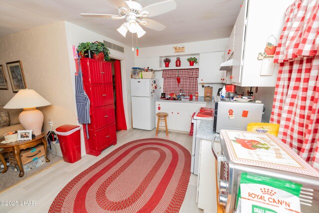 kitchen with light wood finished floors, freestanding refrigerator, white cabinetry, and visible vents