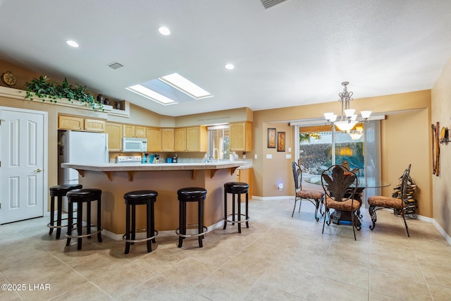 kitchen featuring pendant lighting, light countertops, visible vents, light brown cabinetry, and white appliances