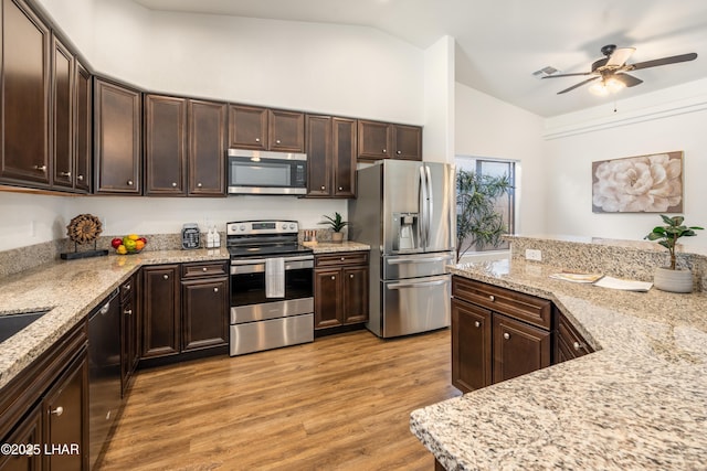 kitchen with lofted ceiling, dark brown cabinetry, stainless steel appliances, light stone countertops, and light wood-type flooring