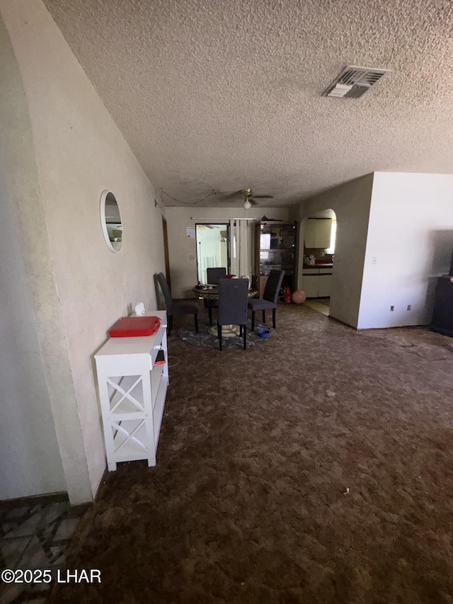 dining area featuring a ceiling fan, a textured ceiling, visible vents, arched walkways, and carpet