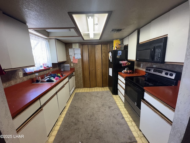 kitchen with visible vents, light floors, black appliances, and white cabinets