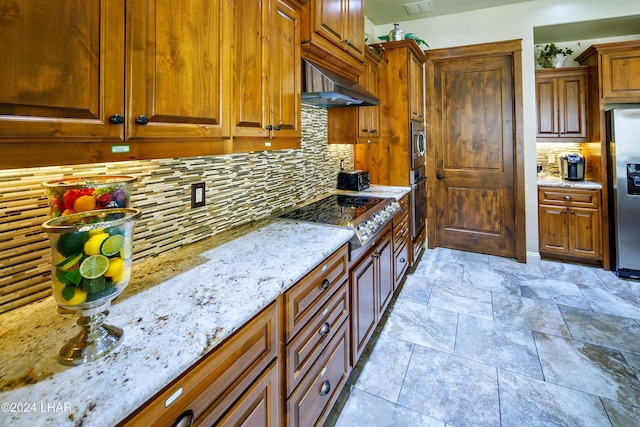 kitchen featuring light stone counters, backsplash, wall chimney exhaust hood, and appliances with stainless steel finishes