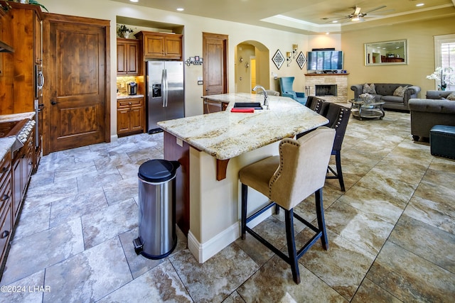 kitchen with appliances with stainless steel finishes, sink, a kitchen bar, a tray ceiling, and a center island with sink