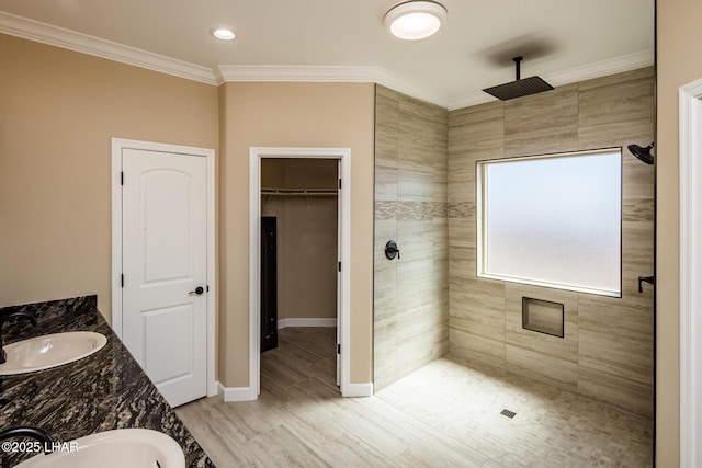 bathroom featuring a sink, a spacious closet, crown molding, and a tile shower