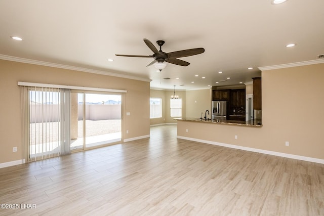 unfurnished living room with crown molding, baseboards, ceiling fan with notable chandelier, light wood-style floors, and a sink