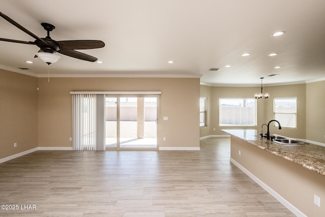 unfurnished living room with ornamental molding, ceiling fan with notable chandelier, a sink, recessed lighting, and baseboards