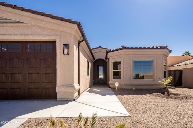 view of exterior entry featuring stucco siding, a tiled roof, and a garage