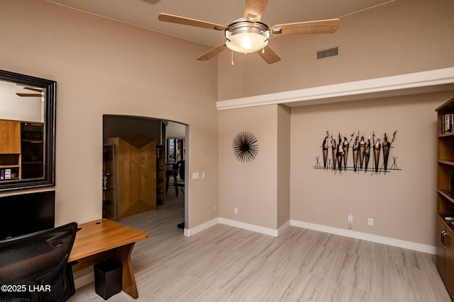 office area with arched walkways, wood finished floors, a ceiling fan, visible vents, and baseboards