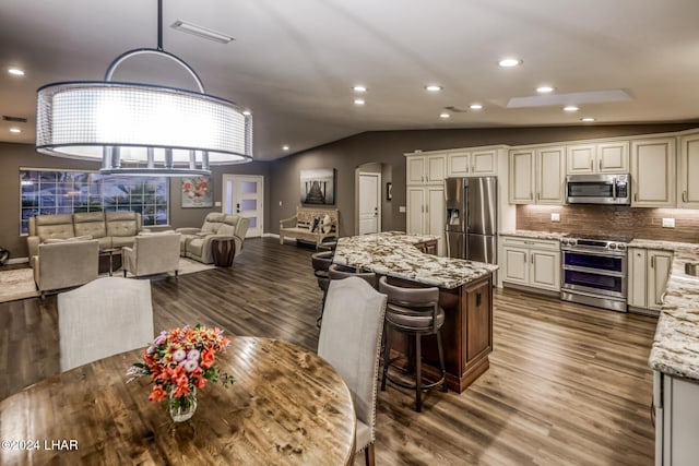 kitchen with vaulted ceiling, dark hardwood / wood-style floors, pendant lighting, light stone counters, and stainless steel appliances