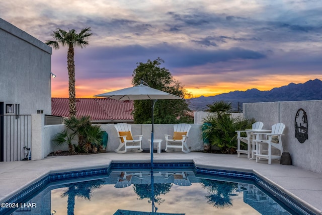 pool at dusk featuring a mountain view and a patio area