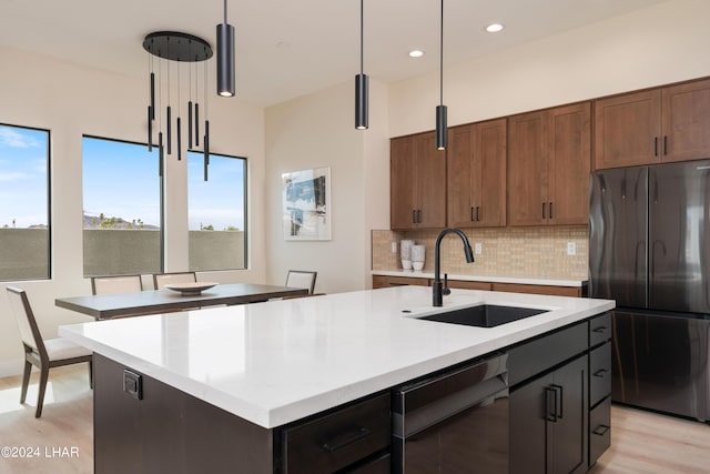 kitchen featuring stainless steel fridge, decorative light fixtures, sink, and a center island with sink