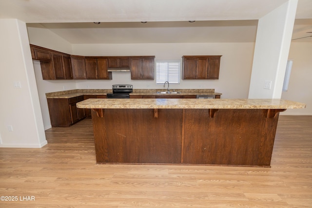 31447 Marine Dr, Parker, AZ 85344 - kitchen with light wood-style flooring, a kitchen bar, stainless steel range with electric stovetop, under cabinet range hood, and a sink