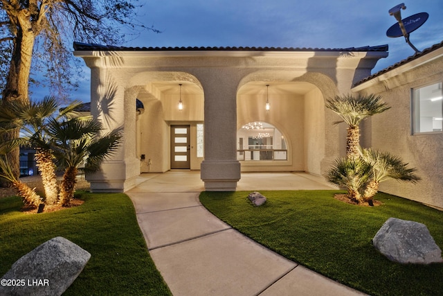 view of exterior entry featuring a patio, a lawn, and stucco siding