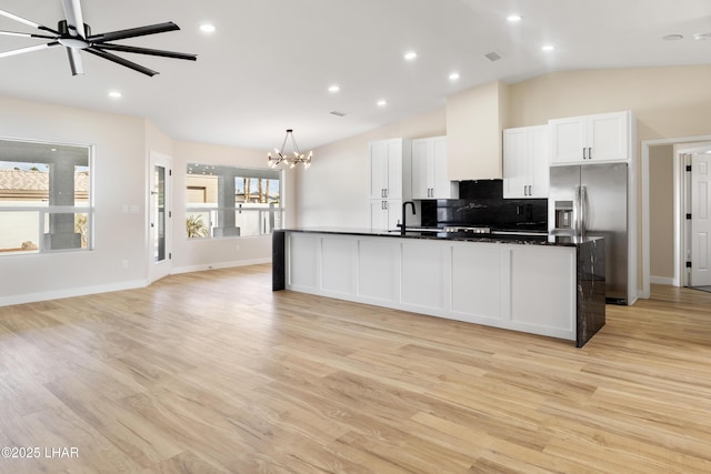 kitchen with white cabinetry, vaulted ceiling, stainless steel refrigerator with ice dispenser, an island with sink, and dark countertops