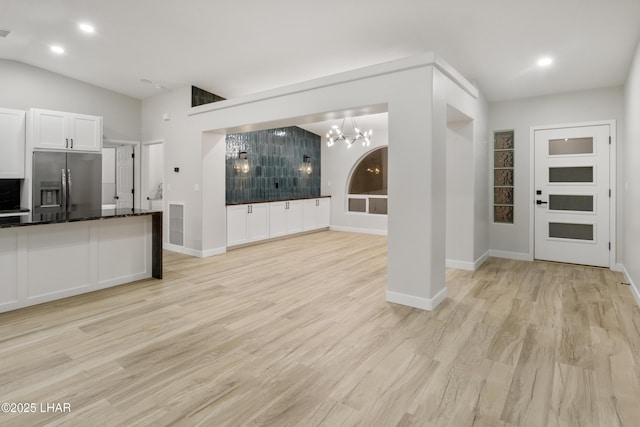 kitchen with light wood-style floors, white cabinets, vaulted ceiling, a chandelier, and stainless steel fridge